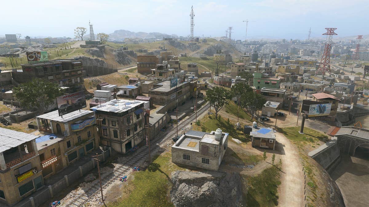 Warzone's Urzikstan map. Buildings sit in front of a hill, with a track cutting through the middle.