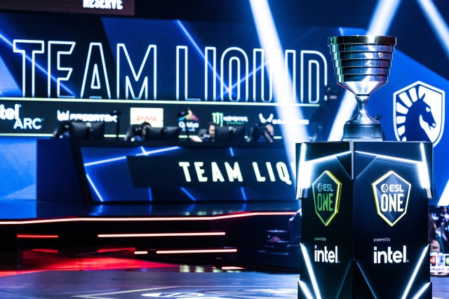 The ESL One Birmingham trophy sits to the front right of the image on stage. Behind, Team Liquid are competing