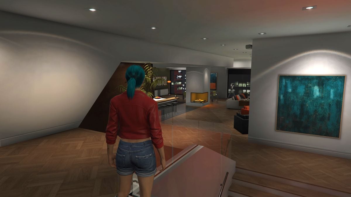 Image of a player character standing in her apartment. She is wearing a red leather jacket and denim shorts. The background consists of a modern-looking apartment with a blue streaked painting hung on a right-angled wall next to a window. There is also a fireplace and a kitchen area in the room.