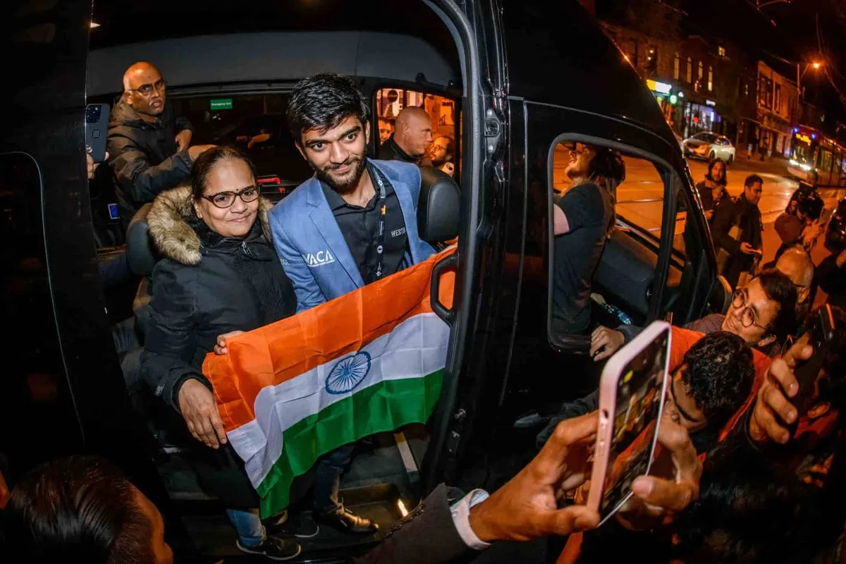Gukesh poses with the Indian flag amidst a scrum of fans.