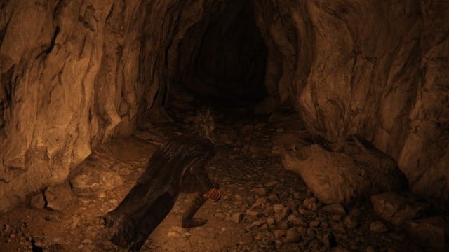 A Tarnished wearing black armor like Batman sneaks down a cave.