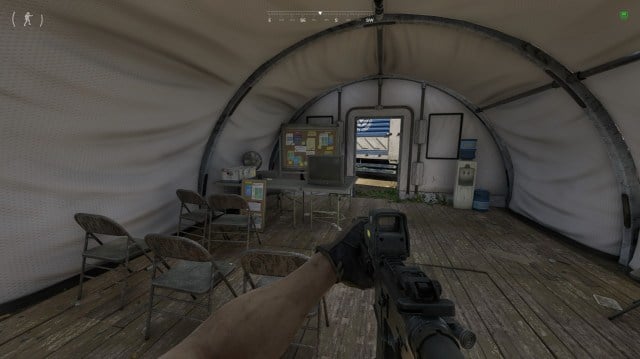 A player holds a rifle in a medical tent in Gray Zone Warfare, looking at a TV.