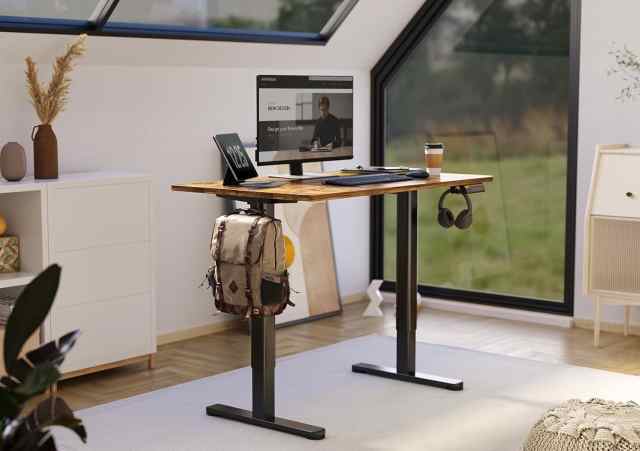 Claiks Electric Standing Desk with a monitor on top, backpack and headset hanging from it, in a white room