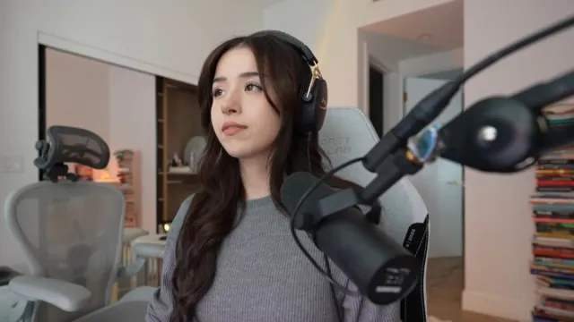 Pokimane sits at her desk, wearing headphones. A microphone is in front of her, and her eyes are focused on her screen.