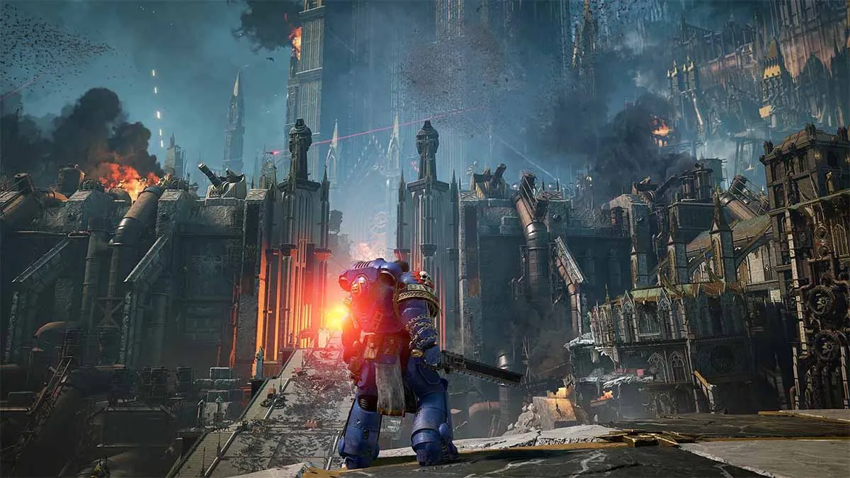 A character in bulky blue armor looks towards a gate, with a tower-like structure behind it. There is gunfire all around.