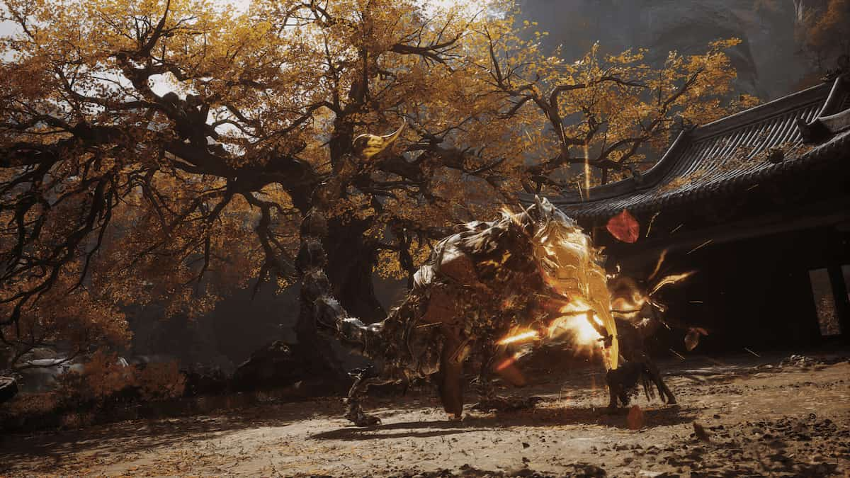 Wukong in Black Myth Wukong fighting against a four-legged creature with a golden glowing head in front of a medieval house beside a yellow tree.