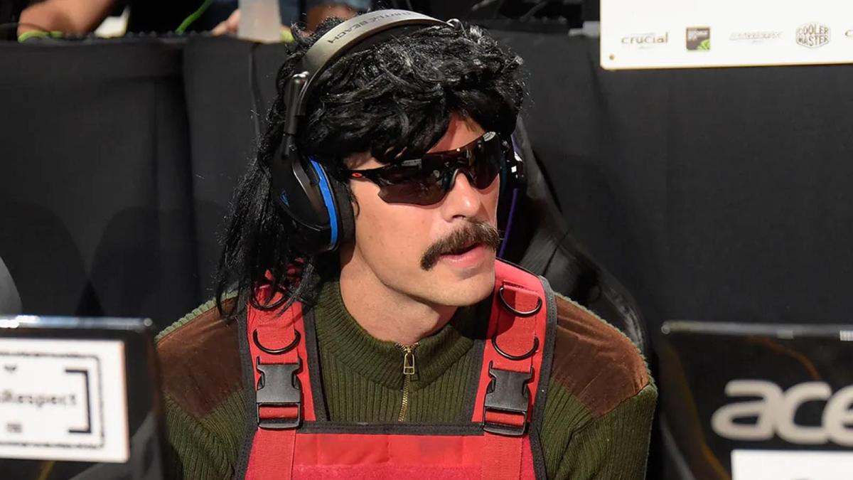 Dr Disrespect appears dressed in a red vest and camo jumper at an esports event