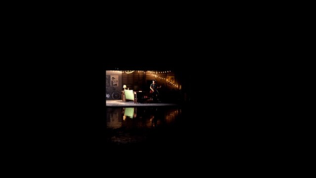 Linda's memory of Bonnie playing on her guitar in the garage, surrounded by a black void with water on the ground as we approach the memory from afar