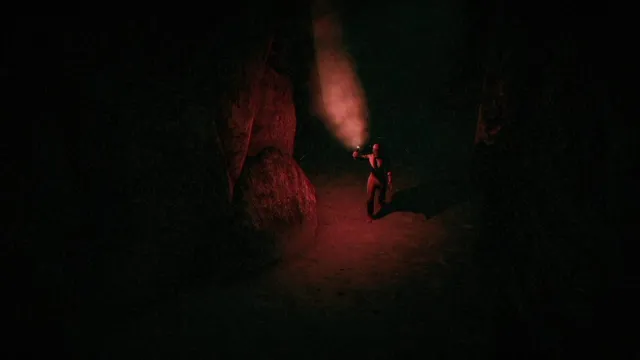 Sasha walking through a pitch black cave with her flare lit to illuminate the way