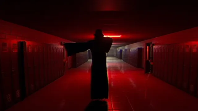 The Cloaked Figure pointing with red light illuminating in the background of The Classrooms