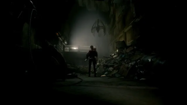 A dark wide shot of Claire with her back to the camera, carrying Sherry in the garbage room