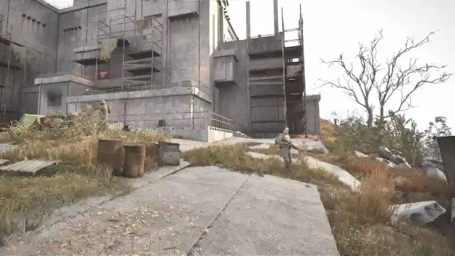 A man with a rifle walks outside of broken down, dilapidated buildings.