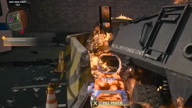 A player looking between a barricade and a destroyed tank towards a burnt-out car.