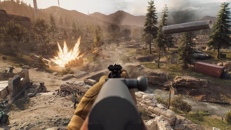 An operator aims down the iron sight of a rifle as an explosion goes off in a wooded battlefield before them.