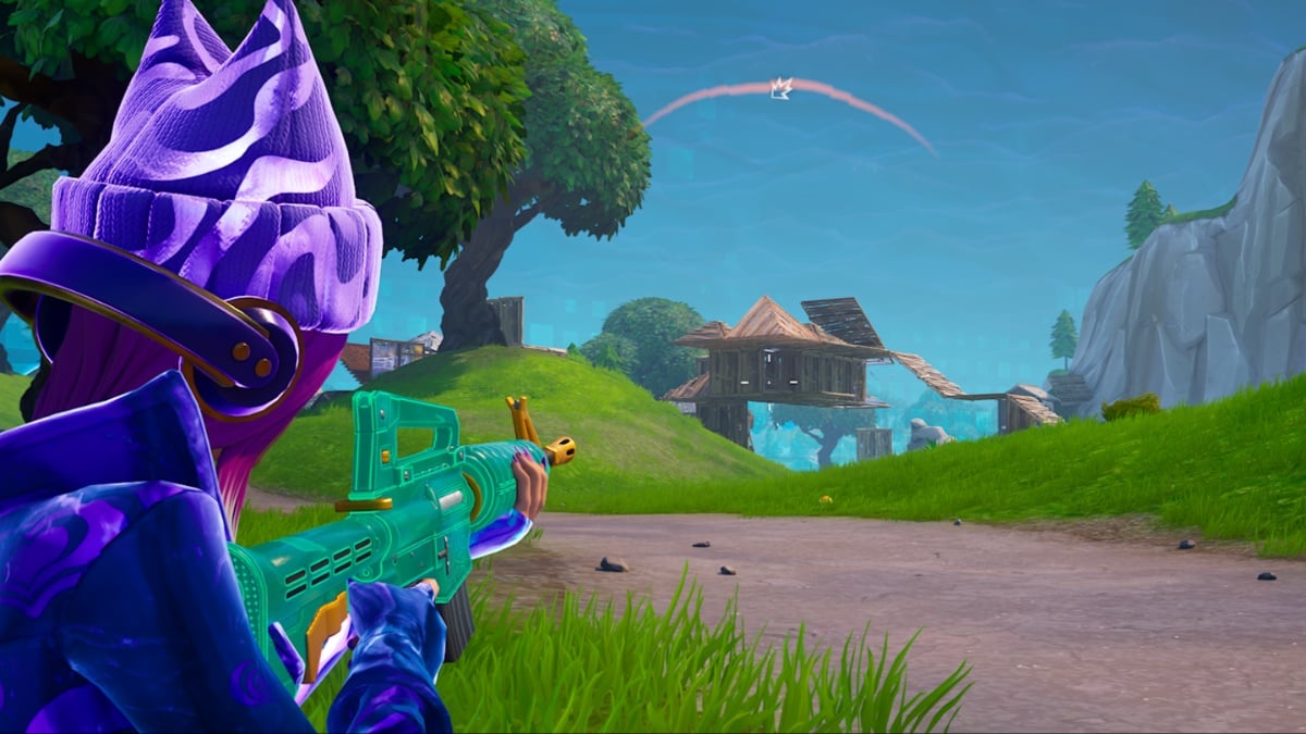 Fortnite character in purple hat pointing green gun at a build