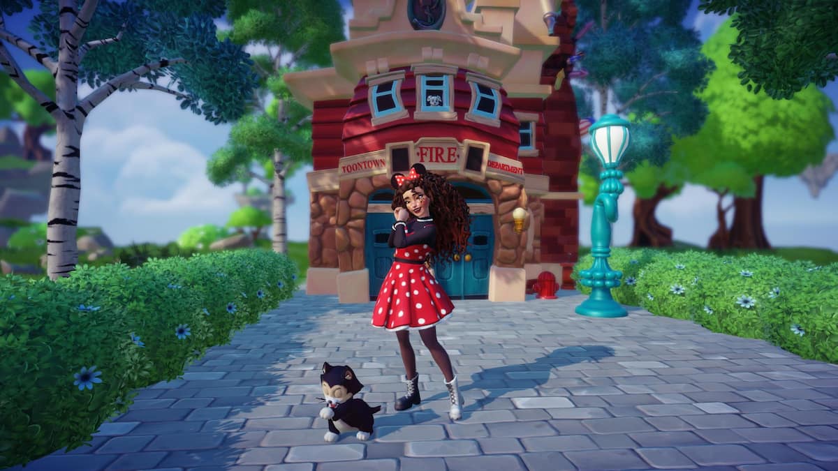 A player with curly hair and black and red minnie ears wearing a red, white, and black polka dot dress staring down at a black and white cat while standing in front of the Toontown fire station in Disney Dreamlight Valley.