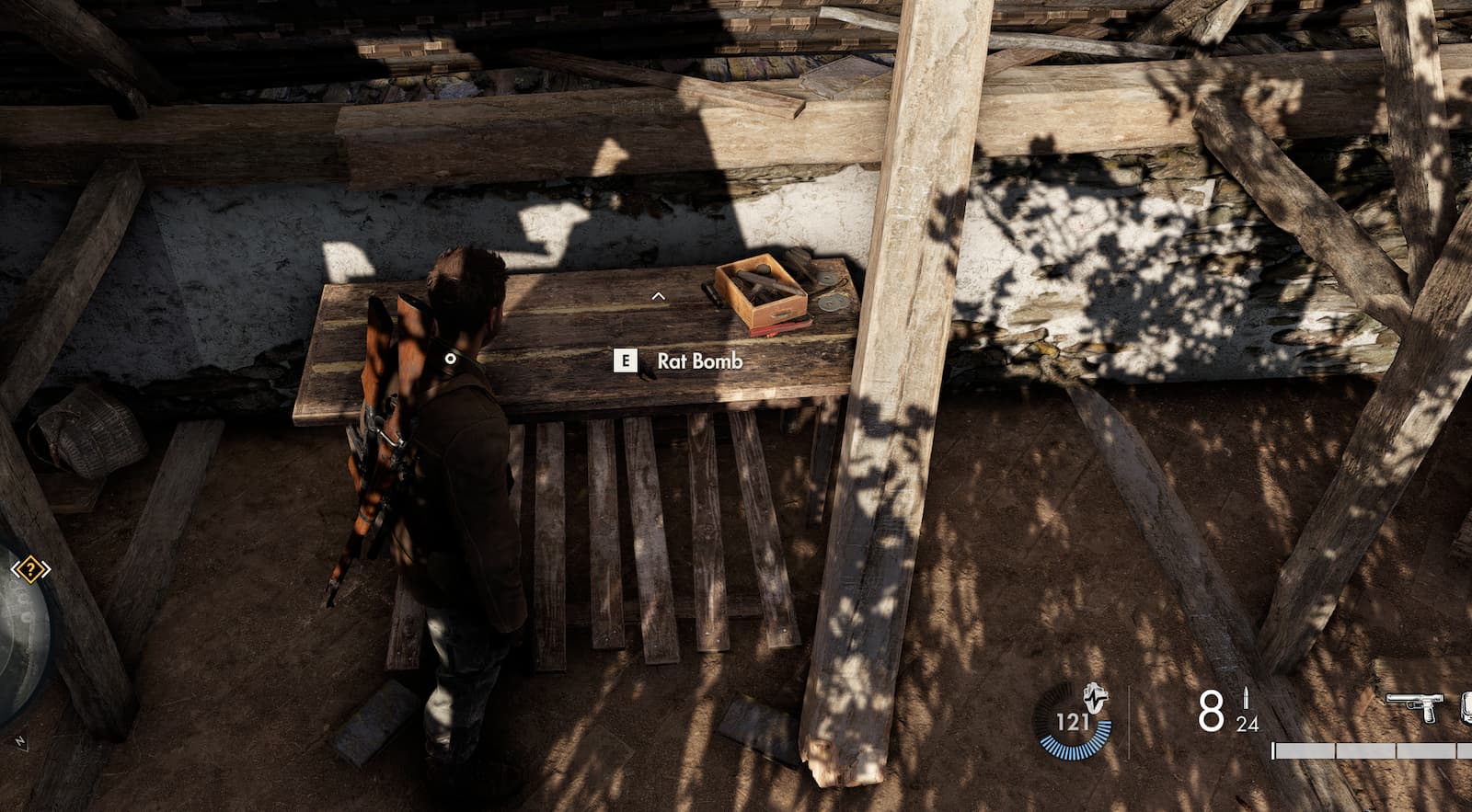 Harry, the main character from Sniper Elite Resistance, stands in front of a wooden table with a rat bomb on top of it.