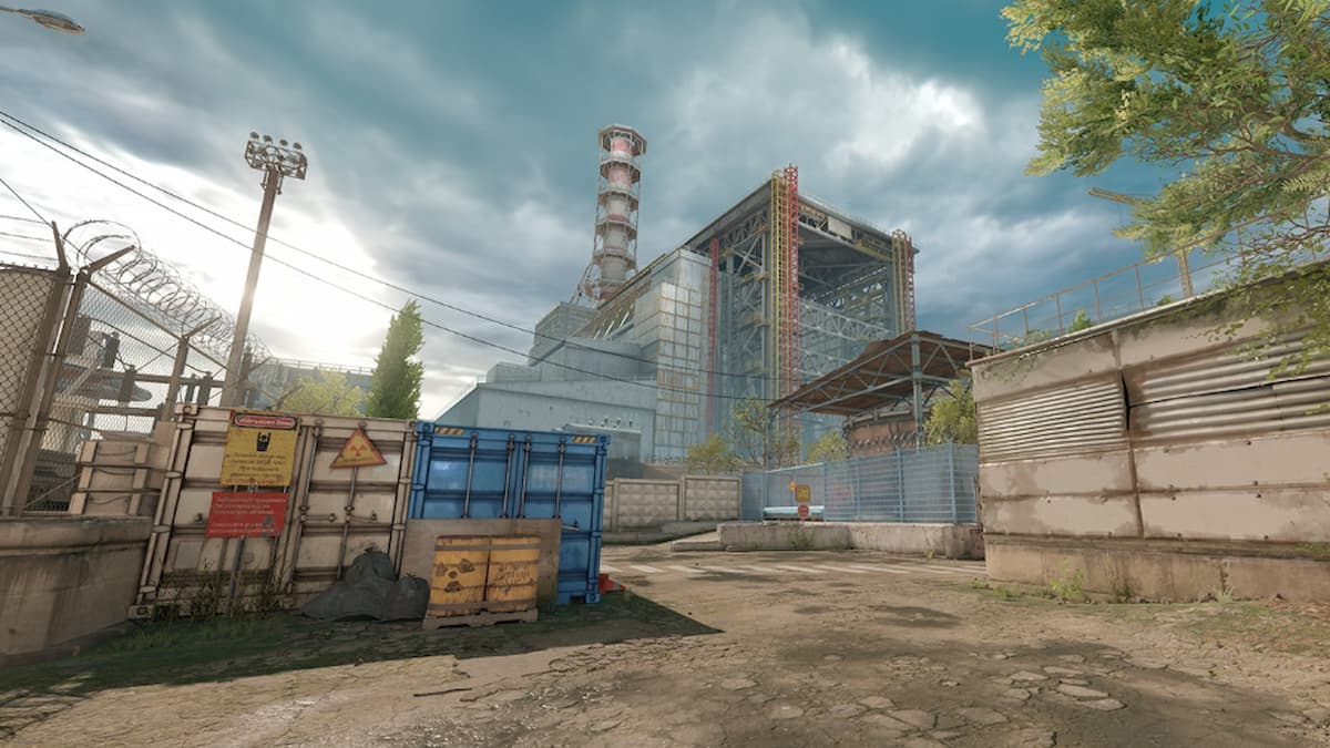 View of the Terrorist spawn site in CS2's Cache with the Chornobyl Power Plant visible in the distance and various containers and radioactive barrels laying around.