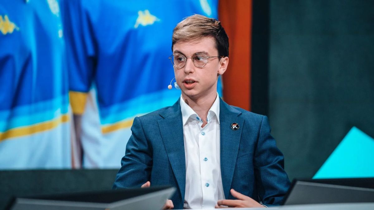 Caedrel wearing a formal dress as he serves on the desk during a League of Legends tournament.