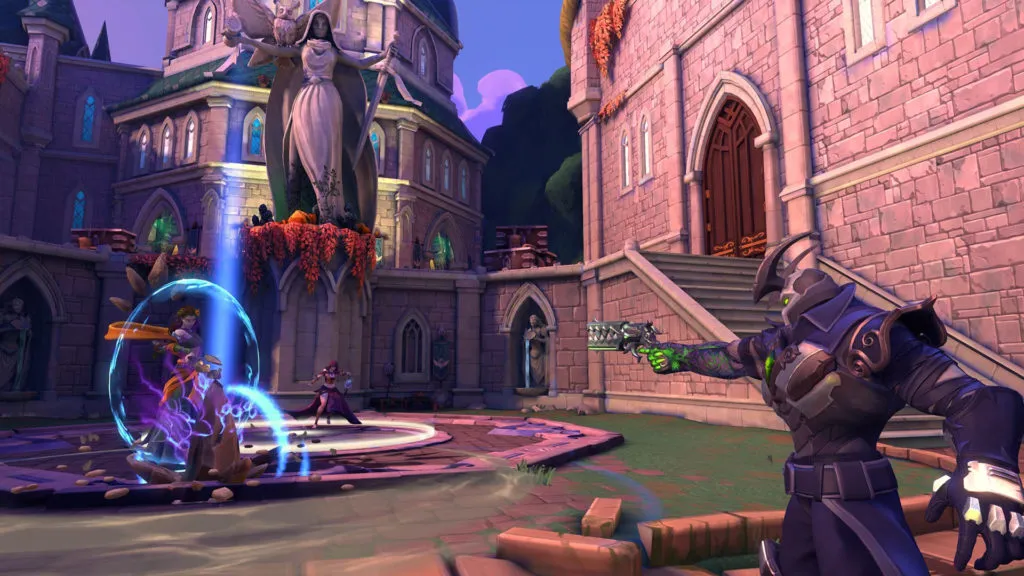 A character aims a green pistol at another character surrounded by a shield in an open town square, with an angelic-like fountain and a small castle in the backdrop in Paladins.