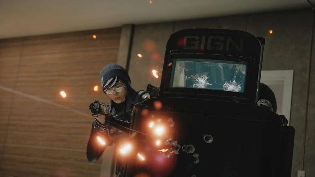 An enemy soldier swings out from behind a riot shield and shoots back at an enemy in Rainbow Six: Siege.